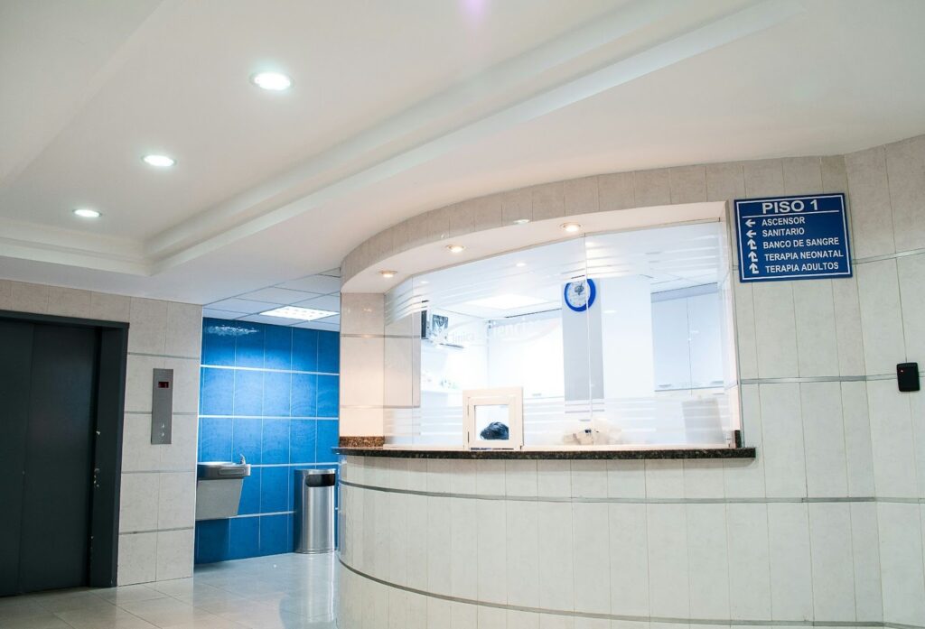 Interior view of a modern medical clinic lobby with blue tiled walls, recessed lighting, and clear wayfinding signage.