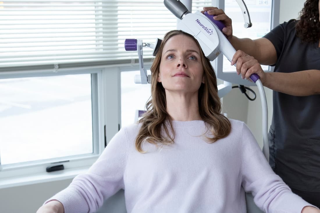 TMS vs Spravato with a calm woman receiving a NeuroStar TMS session administered by a clinical technician.