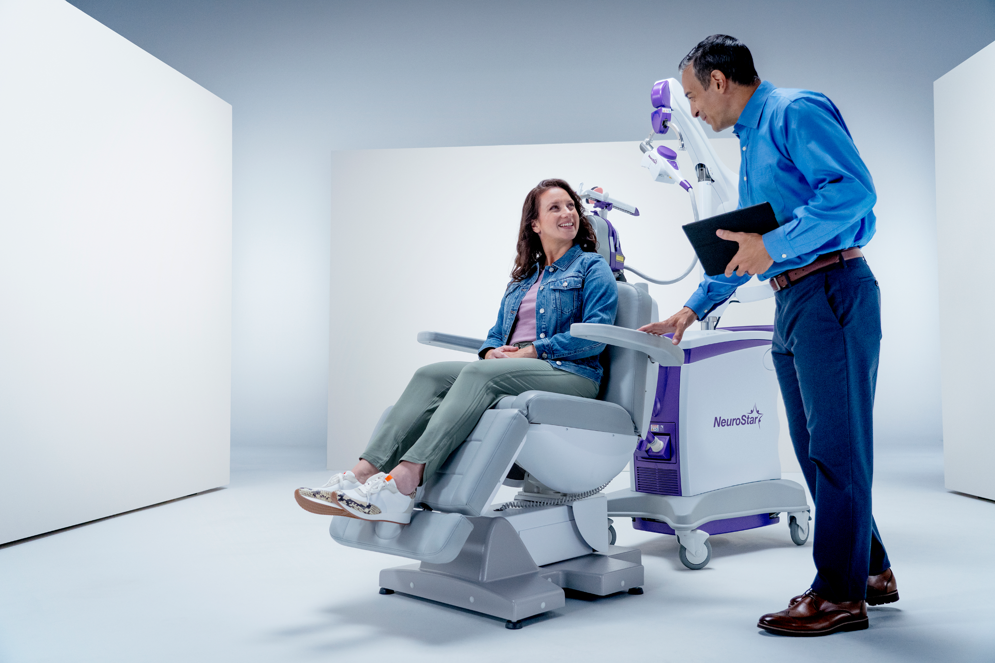 A doctor speaking with a patient in a medical chair about how TMS works for anxiety.