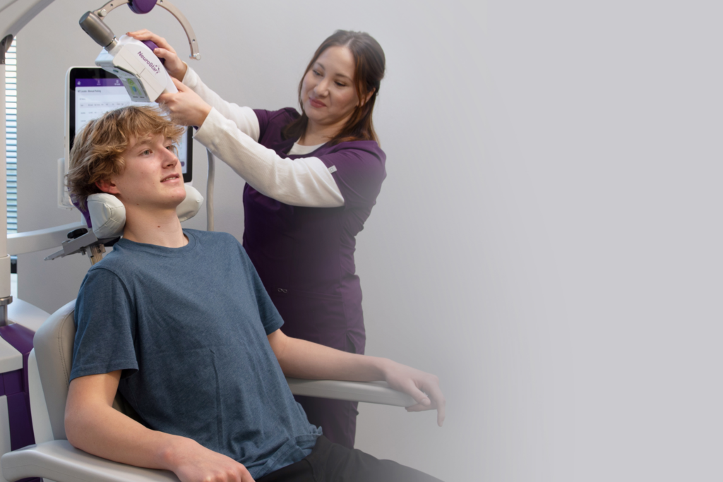 A practitioner adjusting a NeuroStar TMS coil on a teenage boy sitting comfortably in a medical chair.
