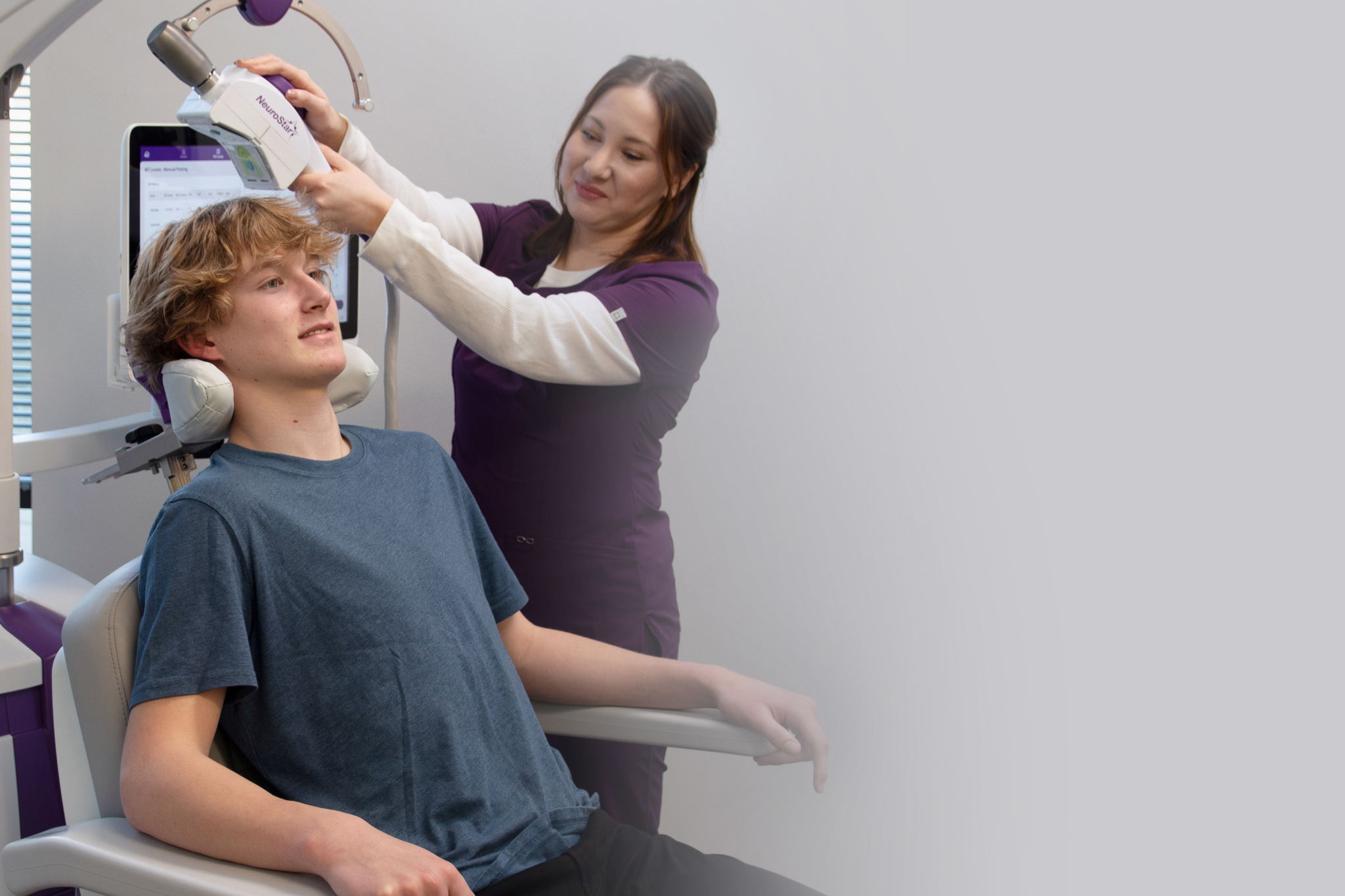 A practitioner adjusting a NeuroStar TMS coil on a teenage boy sitting comfortably in a medical chair.